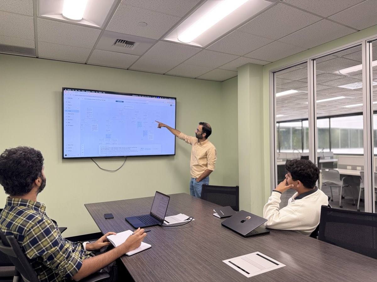 Three teammates in a conference room, one pointing at a triage canvas on the wall screen